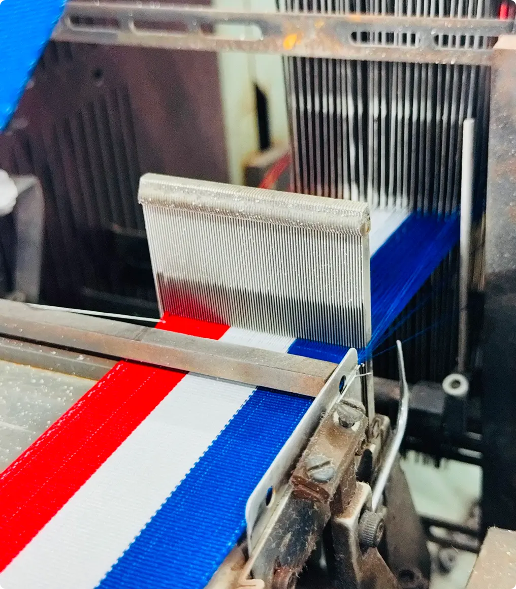 Métier à tisser en production, peigne et fils de chaîne au-dessus d’un ruban bleu, blanc et rouge — Maison Satab