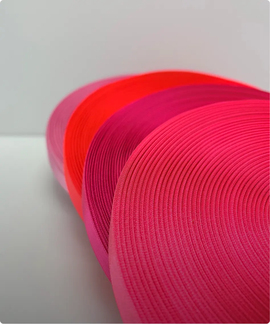 Quatre rouleaux de rubans gros-grain déroulés, du rose fuchsia au rouge fluo, sur fond clair — Maison Satab