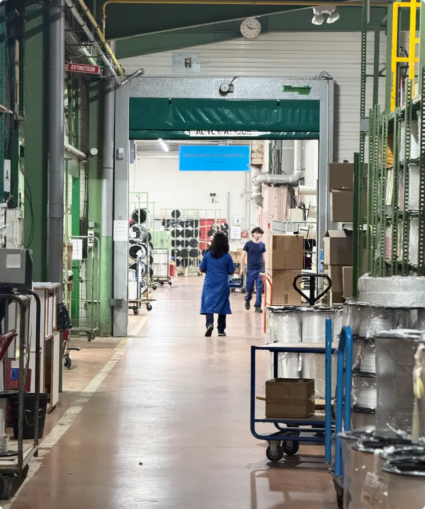 Allée de l’atelier de production Maison Satab, deux personnes au travail parmi les machines — Maison Satab