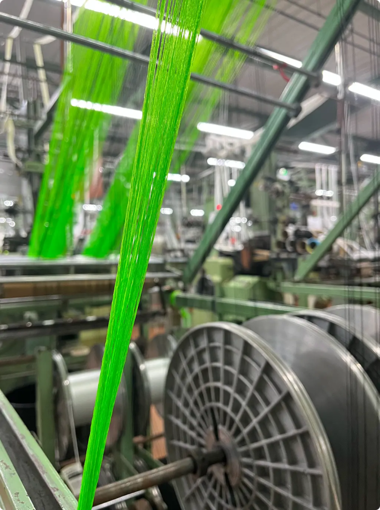 Métier à tisser en fonctionnement, faisceau de fils vert fluo tendus vers le peigne — Maison Satab