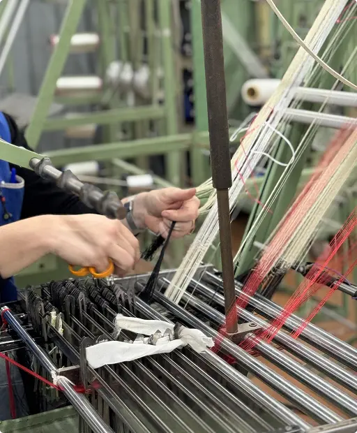 Mains d’un opérateur réglant les fils de chaîne sur un métier à tisser — Maison Satab