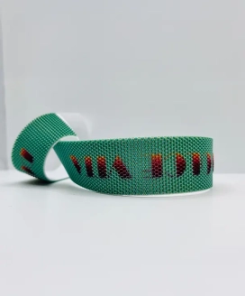 Sangle tissée vert émeraude animée d’un motif jacquard rouge, enroulée sur fond clair — Maison Satab